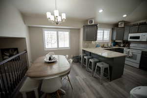 Kitchen with a sink, white appliances, a kitchen breakfast bar, a chandelier, and a peninsula