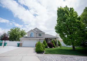 View of front facade featuring a garage, fence, a front lawn, concrete driveway, and stucco siding