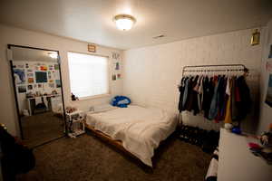 Bedroom featuring carpet floors, a textured ceiling, brick wall, and visible vents
