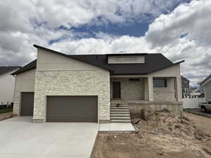 Contemporary house featuring stone siding, driveway, a garage, and a porch