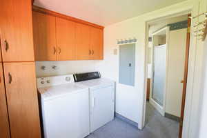 Washroom with separate washer and dryer, cabinet space, light carpet, electric panel, and baseboards