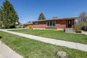 Single story home with concrete driveway, a chimney, a front yard, brick siding, and a garage