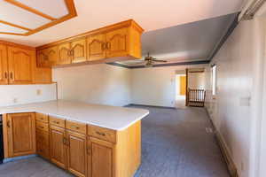 Kitchen with light countertops, carpet, brown cabinets, a ceiling fan, and a peninsula