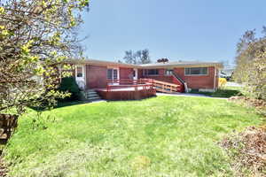 Rear view of property featuring a lawn, a deck, and brick siding