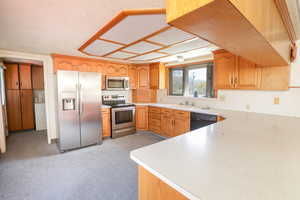 Kitchen featuring brown cabinetry, appliances with stainless steel finishes, light countertops, and a sink