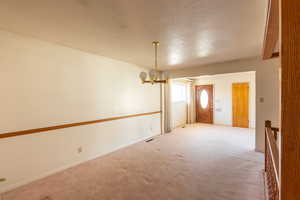 Empty room with an inviting chandelier, carpet, and a textured ceiling