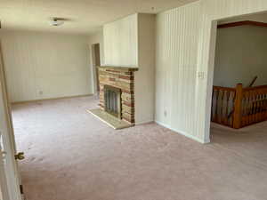 Unfurnished living room featuring light colored carpet, a textured ceiling, a stone fireplace, and baseboards