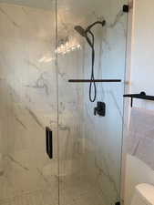 Full bath with a marble finish shower and toilet
