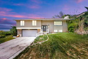 Bi-level home featuring a front yard, a chimney, brick siding, an attached garage, and driveway