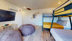 Bedroom with wood finished floors, a wall mounted air conditioner, recessed lighting, and baseboards