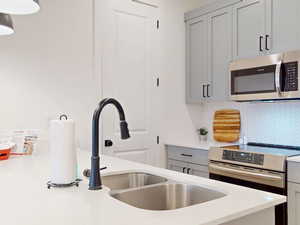 Kitchen with decorative backsplash, stainless steel appliances, light countertops, a sink, and gray cabinetry