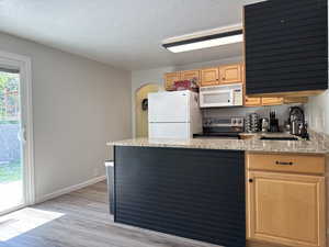 Kitchen with a sink, visible vents, light brown cabinetry, light wood finished floors, and white appliances