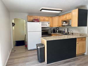 Kitchen with a sink, light brown cabinets, a peninsula, white appliances, and arched walkways