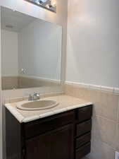 Bathroom with tile walls, visible vents, wainscoting, and vanity