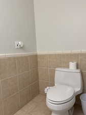 Bathroom with tile patterned floors, toilet, a wainscoted wall, and tile walls