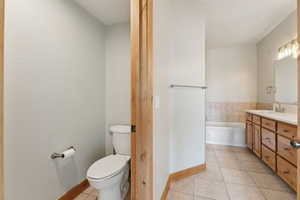 Master Bathroom with double sinks, quartz countertop, walk-in closet, tile patterned floors, toilet and a garden tub