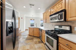 Kitchen featuring quartz countertops, tasteful backsplash, stone finish floor, appliances with stainless steel finishes, a sink, and a peninsula