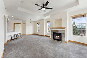 Unfurnished living room with gas fireplace, a raised ceiling, a ceiling fan, and carpet floors