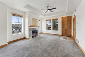 Unfurnished living room featuring a gas fireplace,  raised ceiling, a wealth of natural light, and carpet floors