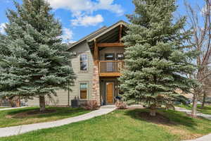 View of front of house with a front yard, central air condition unit, and a balcony