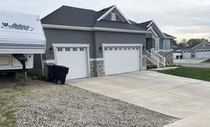 View of side of property featuring stucco siding, a shingled roof, a garage, stone siding, and concrete driveway