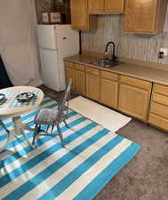Kitchen with carpet floors, freestanding refrigerator, light countertops, wood walls, and a sink