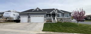 Craftsman-style house featuring driveway, stone siding, a front yard, stucco siding, and a garage