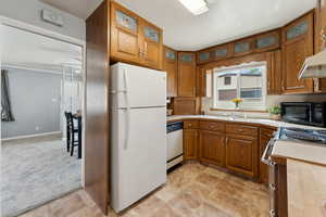 Kitchen with brown cabinets, a sink, white appliances, light countertops, and glass insert cabinets