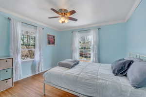 Bedroom featuring ceiling fan, baseboards, ornamental molding, and wood finished floors