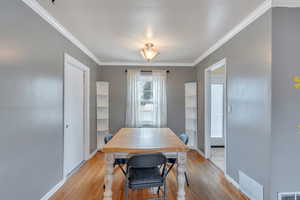 Dining space with baseboards, visible vents, ornamental molding, and light wood-style floors