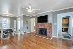 Living area featuring a fireplace, wood-type flooring, baseboards, visible vents, and ornamental molding