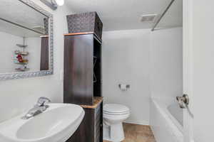Bathroom featuring visible vents, a sink, a textured ceiling, and toilet