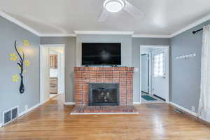 Unfurnished living room featuring ceiling fan, visible vents, a fireplace, wood finished floors, and ornamental molding