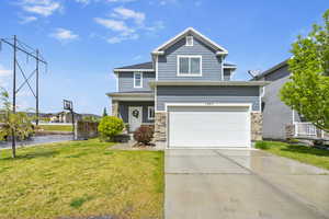 View of front of property with fence, a front yard, stone siding, an attached garage, and driveway