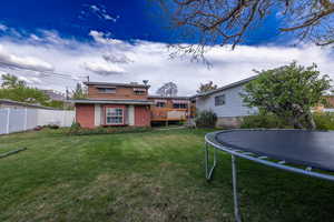 Back of house featuring fence, a trampoline, a lawn, and a deck