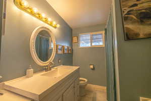 Bathroom featuring vanity, baseboards, lofted ceiling, and toilet