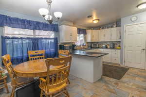 Kitchen featuring stone tile flooring, a peninsula, white cabinetry, stainless steel microwave, and backsplash