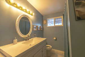 Full bathroom with toilet, baseboards, vaulted ceiling, and vanity