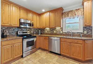 Kitchen with stainless steel appliances, backsplash, recessed lighting, light stone finish floors, and a sink