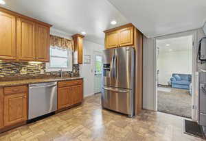 Kitchen with appliances with stainless steel finishes, light stone finish flooring, recessed lighting, tasteful backsplash, and brown cabinetry