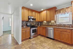 Kitchen featuring a sink, stone tile flooring, tasteful backsplash, baseboards, and appliances with stainless steel finishes
