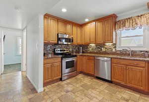 Kitchen with appliances with stainless steel finishes, a sink, decorative backsplash, recessed lighting, and light stone finish floors