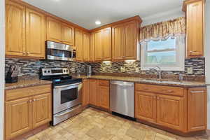 Kitchen with tasteful backsplash, stainless steel appliances, dark stone counters, and a sink