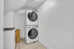 Laundry room featuring cabinet space with sink, light tile patterned floors, baseboards, stacked washer and dryer, and a textured ceiling