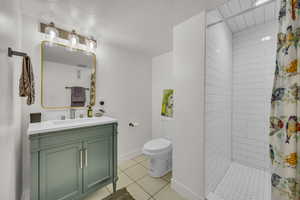 Bathroom with tiled shower, tile patterned flooring, toilet, vanity, and baseboards