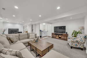 Living area with a fireplace, visible vents, recessed lighting, and light carpet