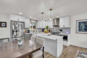 Kitchen with a sink, stainless steel appliances, decorative backsplash, wall chimney range hood, and light countertops