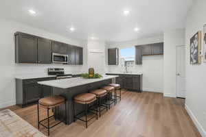 Kitchen with stainless steel appliances, a sink, light wood-style floors, baseboards, and a breakfast bar area