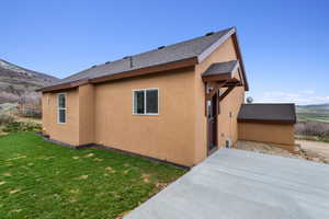 Back of property with a lawn, a mountain view, a patio, a shingled roof, and stucco siding
