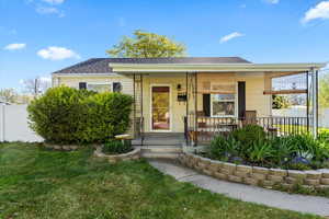 Bungalow-style home featuring a front yard, roof with shingles, covered porch, and fence